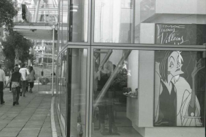 Ein Schwarz-Weiß-Bild von Menschen, die auf einem Boden mit einem Gebäude und einer Wand im Hintergrund stehen.