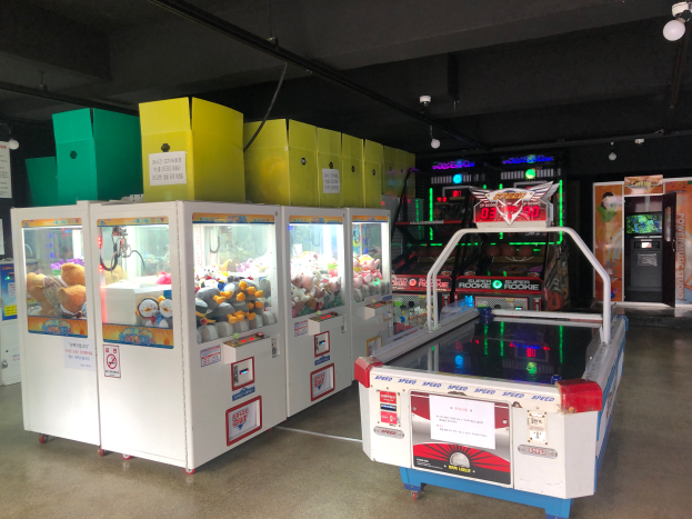 Ein Raum voller verschiedener Arcade-Spiele, mit einem Spielautomaten auf der rechten Seite, einem Boden unten und einer Decke mit Lampen oben.