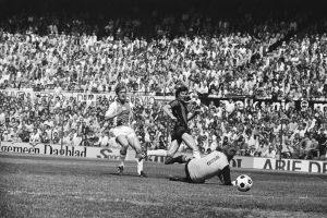 Schwarzes und wei%C3%9Fes Foto von F%C3%BC%C3%9Fballspielern auf einem Feld mit Zuschauern im Hintergrund und einer Bundesliga 1978-79 Ajax 1-1 Hannover 96-Tafel.