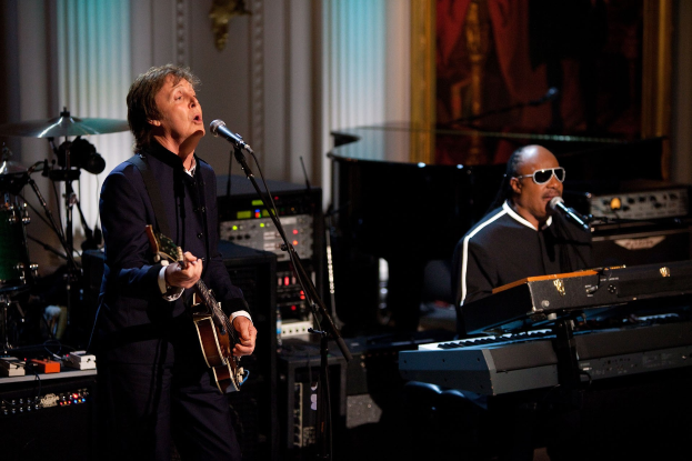 Paul McCartney und Stevie Wonder auf der Bühne, McCartney spielt Gitarre und singt, Wonder trägt eine Schutzbrille und spielt Piano.
