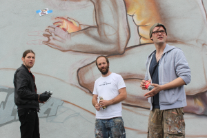 Menschen stehen mit Farbsprühdosen vor einer Wand mit Graffiti.