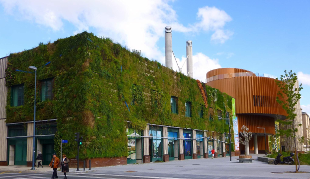 Große nachhaltige Bauweise mit einer Green Wall, umgeben von Straßeninfrastruktur, Fahrzeugen, Fußgängern, Bäumen und einem bewölkten Himmel.