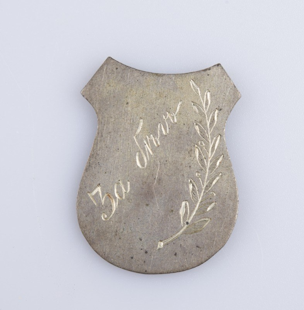 Ein silbernes Abzeichen mit einem Lorbeerkranz, darauf die Inschrift "50. Hochzeitstag", auf einem weißen Hintergrund.