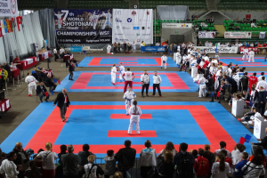 Eine Gruppe von Menschen steht auf einer blauen und roten Judo-Matte bei den 7. World Shotokan Championships in Polen, umgeben von Zuschauern und Bannern.