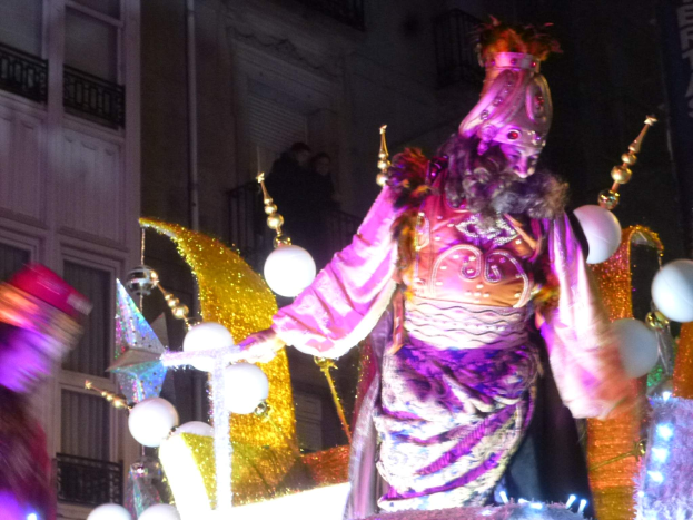 Ein Mann in einem Kostüm steht auf einem dekorierten Festwagen in einem Umzug, mit einem Stadtgebäude im Hintergrund.