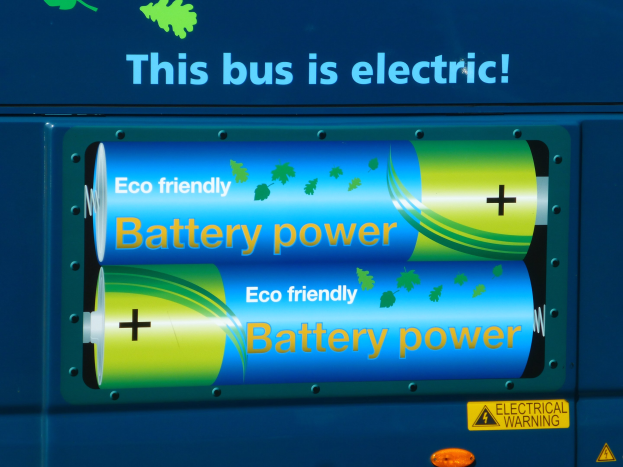 Blauer elektrischer Bus mit "Dieser Bus ist elektrisch"-Schriftzug und zwei sichtbaren seitlich angebrachten Batterien.