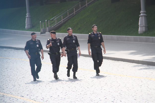 Drei Polizeibeamte in Uniform und Mützen, die eine Straße mit Geländern, Treppen und Gras im Hintergrund hinuntergehen.