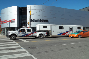 Ein Polizeiwagen parkt vor einem Gebäude mit Text darauf, mit einer Verkehrsampel mit Pfahl und Drähten im Vordergrund und Bäumen und einem klaren blauen Himmel im Hintergrund.