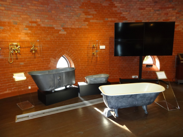 Ein gemütliches Badezimmer mit einer Backsteinwand, einer zentralen Badewanne, an der Wand montierten Wasserhähnen auf der linken Seite und einem an der Wand montierten Fernseher auf der rechten Seite.