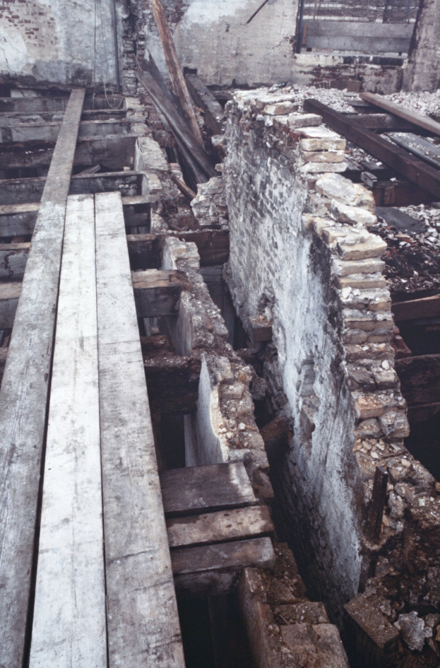 Altbau im Abriss mit verstreuten Holzplanken und Steinen auf dem Boden und einer Wand im Hintergrund.