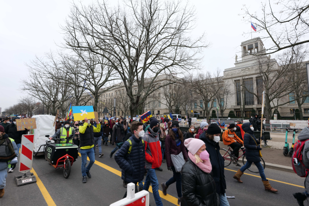 Eine große Gruppe von Menschen marschiert auf der Straße in Washington, D.C. am 21. Januar 2020 mit Schildern und Transparenten, einige fahren Fahrräder, Schilder mit Stangen, Bäume und einen klaren blauen Himmel im Hintergrund.