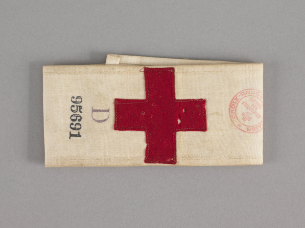 Ein rotes Kreuz-Ersthilfepaket in einem Stoffbeutel mit Text und Stempel, das auf einer Oberfläche liegt.