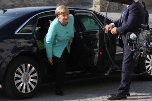 Bundeskanzlerin Angela Merkel verlässt ein Auto vor der Kanzlei in Berlin, trägt eine blaue Jacke und schwarze Hosen und wird von einem Mann in einem schwarzen Blazer, weißem Hemd und blauen Hosen begleitet.