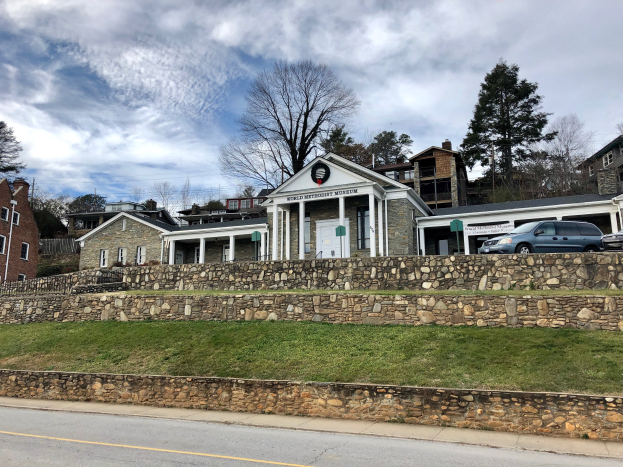Steinwand mit geparkten Autos, benachbarte Gebäude mit Fenstern und Türen, Bäume und ein bewölkter Himmel im Hintergrund, als Weltkulturerbe-Museum bezeichnet.