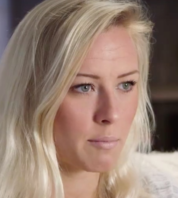 Frau mit langen blonden Haaren und blauen Augen im Vordergrund, die besorgt wirkt mit einem unscharfen Hintergrund.