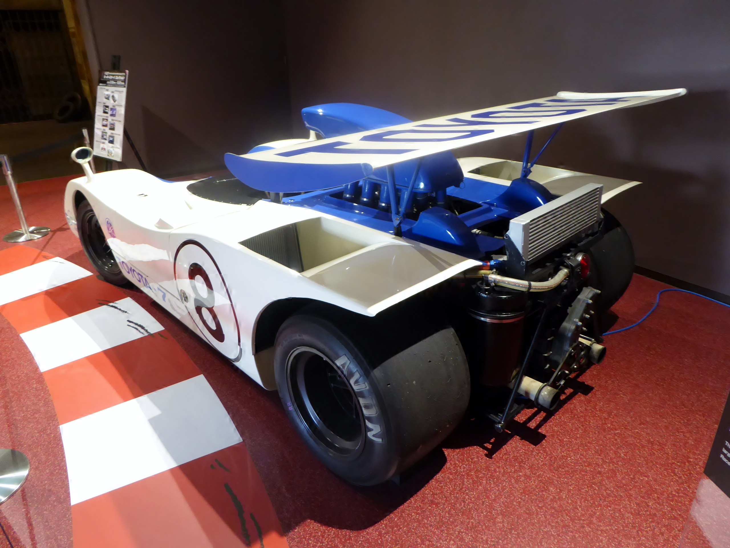 Ein wei├č-blauer Rennwagen in einem Museums Setting auf dem Goodwood Festival of Speed, umgeben von Barrieren und Informationsschildern.