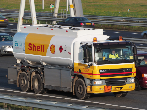 Ein Shell-Tanklastwagen, der auf einer Autobahn mit anderen Fahrzeugen fährt, mit sichtbaren Insassen, umgeben von Leitplanken, Strommasten, Schildern und Gras.