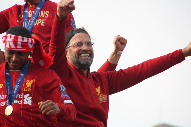 Liverpool-Trainer Jürgen Klopp feiert mit Spielern und Staff nach dem Gewinn der UEFA Champions League, trägt eine rote Jacke mit zwei Medaillengewinnern in einem Stadion.