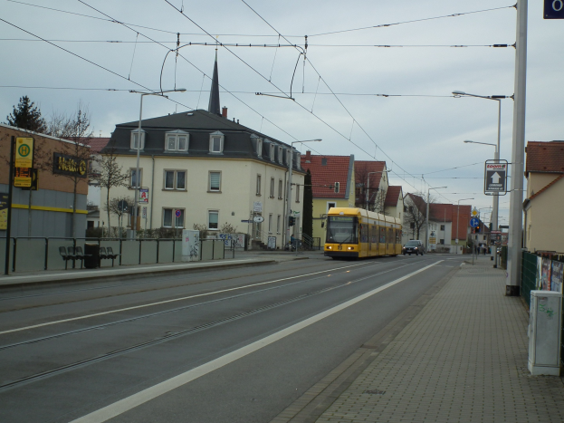 Eine gelbe Straßenbahn fährt durch eine Straße mit hohen Gebäuden, Straßenmöbeln und Bäumen unter einem klaren blauen Himmel.