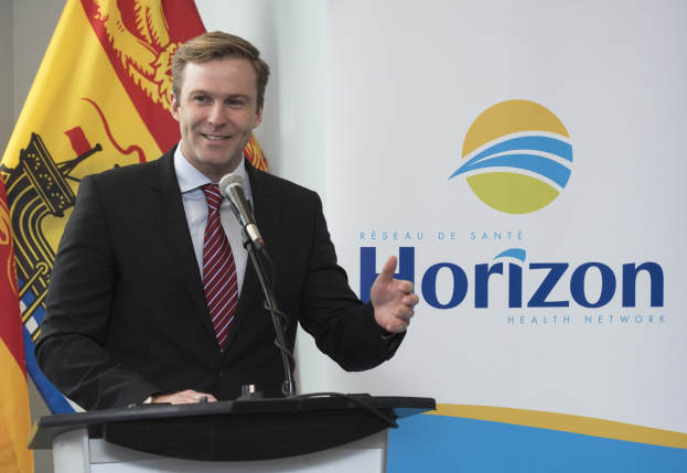 Ein Mann mit einem schwarzen Blazer, einem weißen Hemd und einer roten Krawatte steht an einem Podium mit einem Mikrofon und einem Banner im Hintergrund und spricht als CEO.
