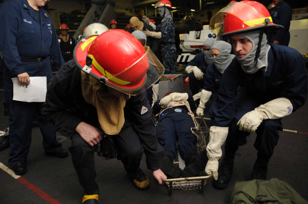 Rettungsteam auf einem Schiffsdeck bei der Unterstützung einer Person auf einer Bahre, wobei eine Person Dokumente hält.