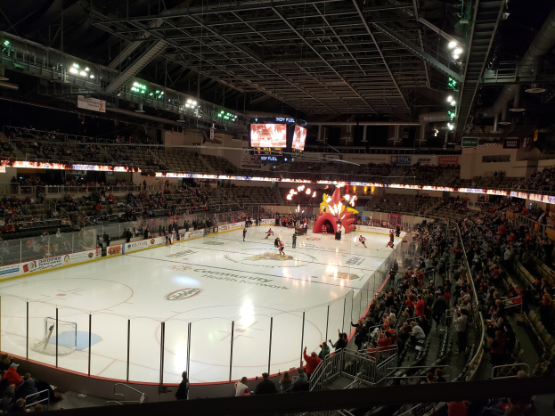 Ein Eishockeyspiel in einer großen Arena mit Zuschauern auf Sitzen und Stehplätzen in der Nähe der Eisfläche, umgeben von Bannern, Metalldachkonstruktionen und zwei Überwachungsschirmen, identifiziert als Nationwide Arena.