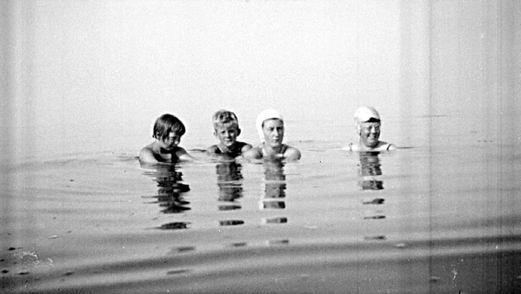 Schwarzes und weißes Foto von vier Kindern, die in einem Pool schwimmen und alle eine Schwimmkappe tragen.