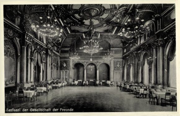 Schwarz-weißes Foto eines großen Raums mit Tischen, Stühlen, Säulen, Bögen und Deckenleuchtern, beschriftet mit "Festival der Gesellschaft der Freunde, Berlin" unten.