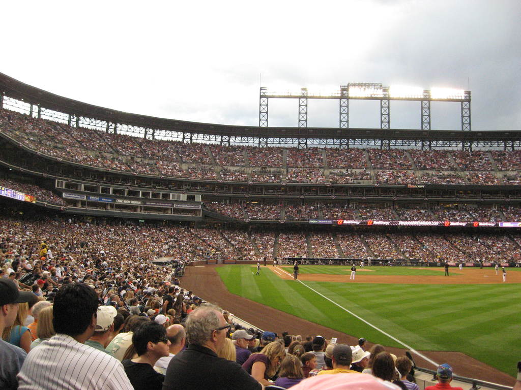 Ein Cricket-Stadion mit Spielern auf dem Feld und Zuschauern in den Rängen, beleuchtet von Scheinwerfern von oben.