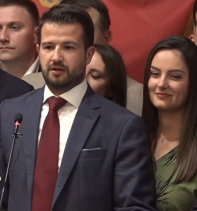 Ein Mann im Anzug spricht an einem Podium mit Mikrofon zu einer Menge hinter einem Banner, wahrscheinlich über ein Regierungssozialmedienverbot.