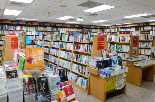 Ein gut sortierter Buchladen mit ordentlich aufgestellten Büchern auf Regalen und Tischen, mit informativen Schildern auf dem Boden und Deckenleuchten.