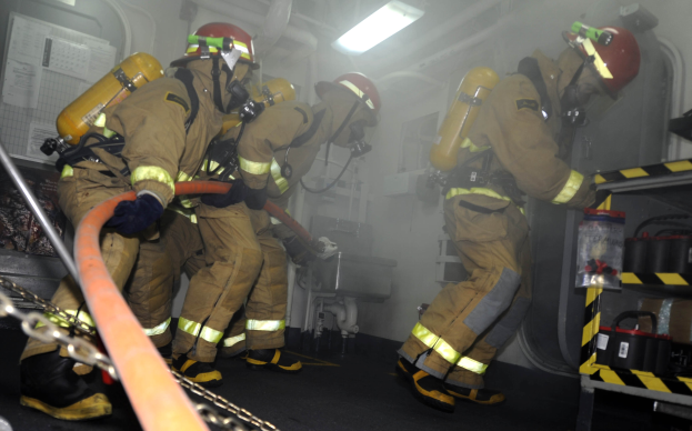 Feuerwehrleute in Schutzausrüstung arbeiten in der Nähe eines Feuerwehrautos mit einem Gestell mit Gegenständen und Hintergrundausrüstung im Hintergrund.