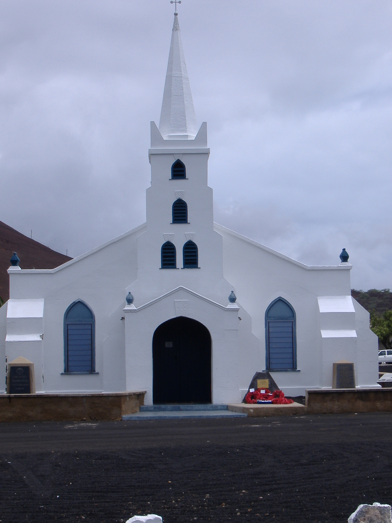 Eine Kirche steht in der Mitte des Bildes, mit einer Straße unten, Bäumen und einem Auto im Hintergrund.