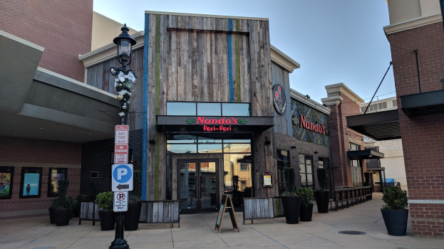 Außenansicht eines Restaurants mit einem Schild, umgeben von städtischen Elementen und einem klaren Himmel.