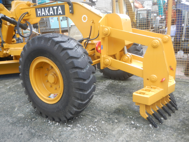 Ein gelber Radlader steht vor einem Gebäude mit einem Metallzaun und einem klaren blauen Himmel.