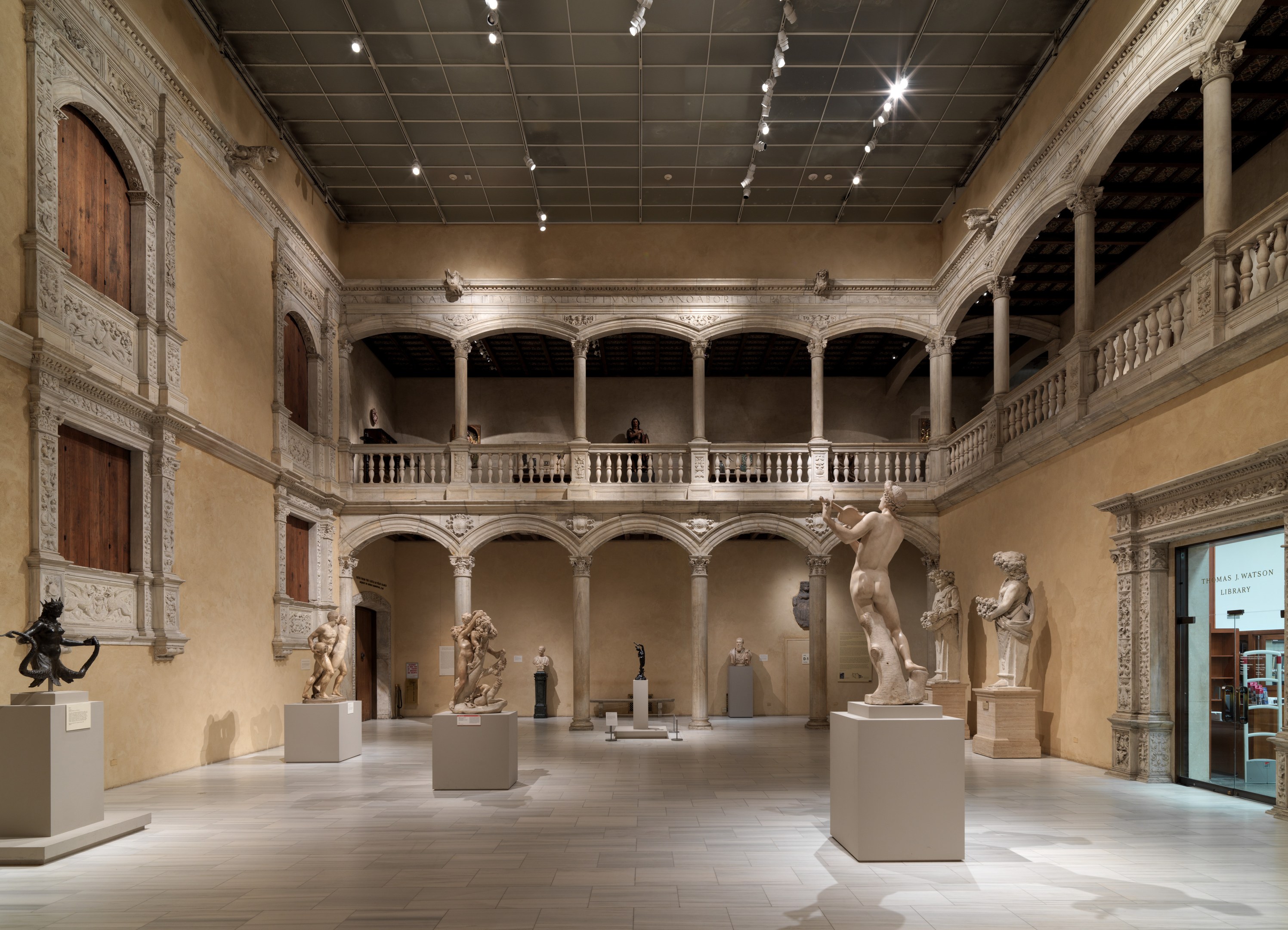 Ein geräumiger Museumsausstellungsraum mit zahlreichen Statuen und Skulpturen auf Sockeln, mit architektonischen Elementen wie Wänden, Säulen, Geländern und einer beleuchteten Decke sowie einigen Besuchern, die die Ausstellungen betrachten.