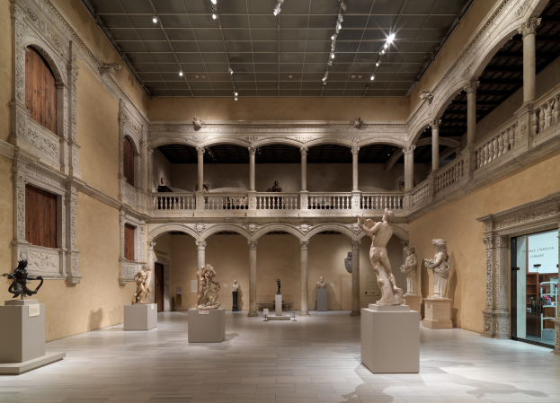 Ein geräumiger Museumsausstellungsraum mit zahlreichen Statuen und Skulpturen auf Sockeln, mit architektonischen Elementen wie Wänden, Säulen, Geländern und einer beleuchteten Decke sowie einigen Besuchern, die die Ausstellungen betrachten.