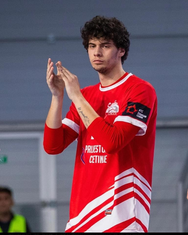 Ein Mann in einem roten und weißen Hemd klatscht in den Händen in der Vordergrund, mit einer anderen Person und einer Wand im Hintergrund, und Text, der 'Kopenhagen Futsal Club - Foto 1' unten liest.
