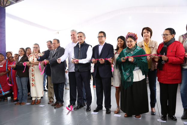 Eine Gruppe von Menschen bei einer Eröffnungszeremonie, die lächeln und eine Schere halten, mit Papieren auf dem Boden und einem weißen Tuch im Hintergrund.