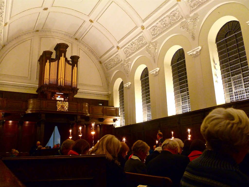 The interior of a church with men and women seated, candles in front of them, and white walls and roof.