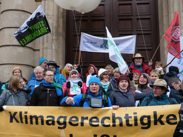 Gruppe von Menschen mit Spruchband, Fahnen und Luftballons vor einem Gebäude mit Säulen während eines Klimastreiks in Deutschland.