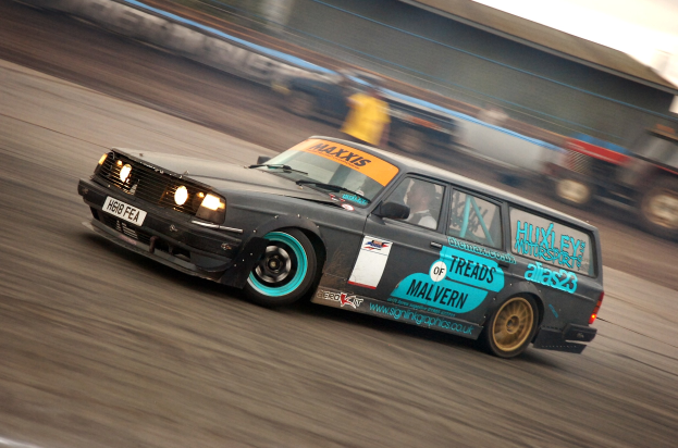 Ein Auto fährt auf einer Rennstrecke, umgeben von anderen Fahrzeugen, mit einer Person darin, der Hintergrund durch die Bewegung unscharf.