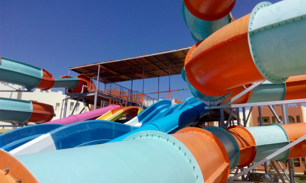 Ein großer Wasserpark mit mehreren bunten Wasserrutschen, Geländern und einem Schuppen, mit Gebäuden und einem klaren blauen Himmel im Hintergrund.