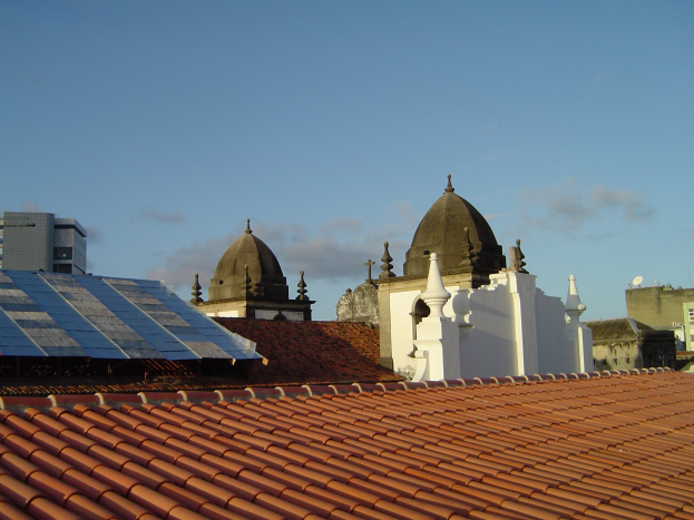 Stadtansicht mit mehreren Gebäuden im Vordergrund, einem blauen Himmel im Hintergrund und Solarpanelen auf einem der Dächer.