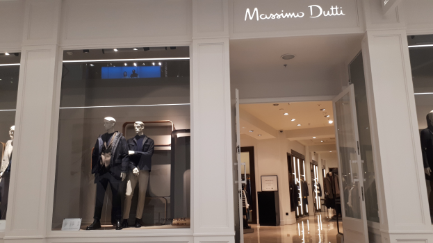 Ein Massimo Dutti Geschäft in Mailand, Italien, zeigt Mannequins in modischer Kleidung, beleuchtete Deckenlampen, Informationsschilder und sichtbaren Boden.