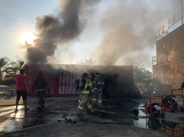 Feuerwehrleute in Schutzausrüstung stehen vor einem brennenden Gebäude und kämpfen gegen die Flammen, während Rauch in den Himmel aufsteigt.