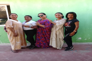 Eine Gruppe von Frauen steht vor einer grünen Wand mit einem Fenster auf der linken Seite und nimmt an einem Internationalen Frauentag teil.