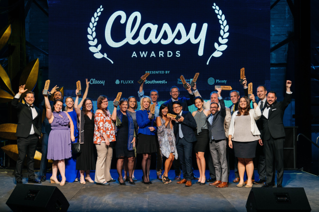 Gruppe von Menschen auf einer Bühne mit Auszeichnungen, Lautsprechern unten und einem Bildschirm mit "Classy Awards 2019" im Hintergrund.