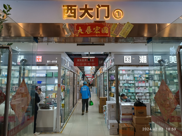 Innenseite einer chinesischen Apotheke mit Glaswänden, Regalen voller Artikel, verstreuten Kartons, einer Pflanze links und einem Schild oben, das darauf hinweist, dass es sich um eine chinesische Drogerie handelt.