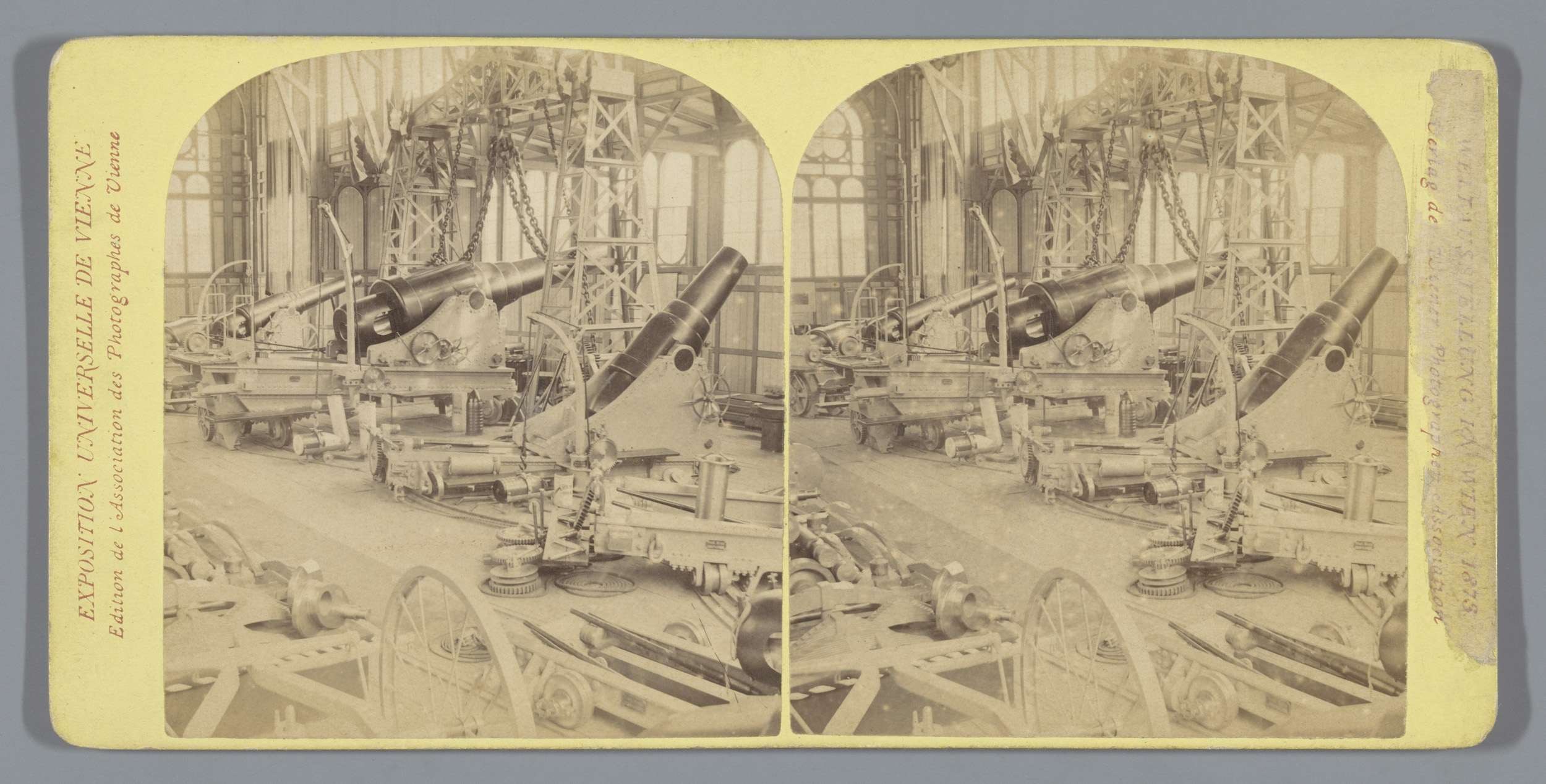 Schwarzes und weißes Foto eines alten Fabrikinneren mit einem gro├čen Geschütz in der Mitte, umgeben von zus├Ątzlichen Geschützen, Metallstangen und verstreuten Gegenst├Ąnden auf dem Boden, mit Text auf der linken Seite.